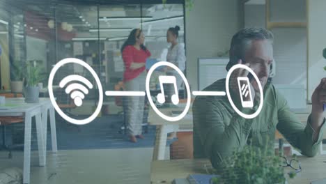 animación de una red de iconos digitales contra un hombre caucásico hablando en un teléfono inteligente en la oficina