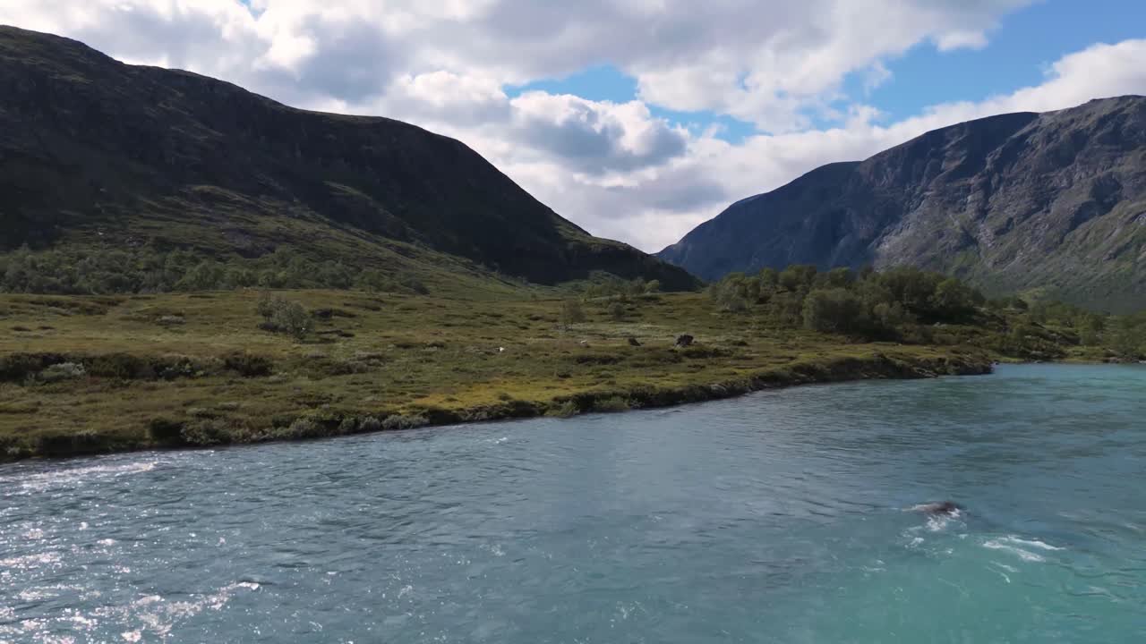노르웨이의 웅장한 산으로 둘러싸인 울창한 계곡을 가로질러 흐르는 푸른색 강은 스칸디나비아 자연의 평온한 아름다움을 보여줍니다.