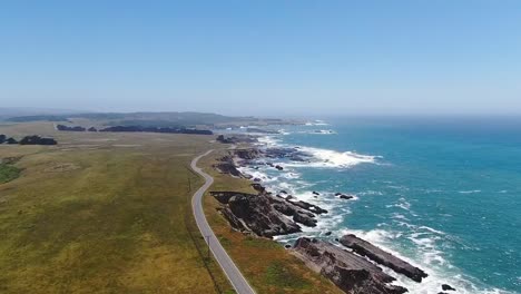 Luftaufnahme-Einer-Wunderschönen-Strandlandschaft-Mit-Einer-Straße-Am-Rande,-Während-Das-Meer-Auf-Die-Felsige-Küste-Trifft