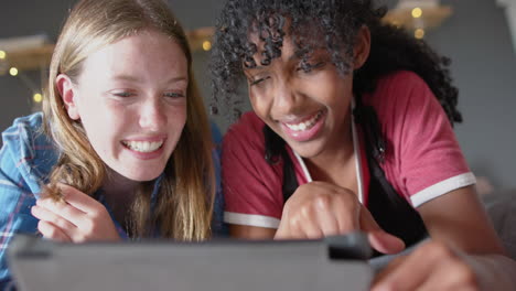 amigas adolescentes felices y diversas acostadas en la cama y usando la tableta en casa, en cámara lenta