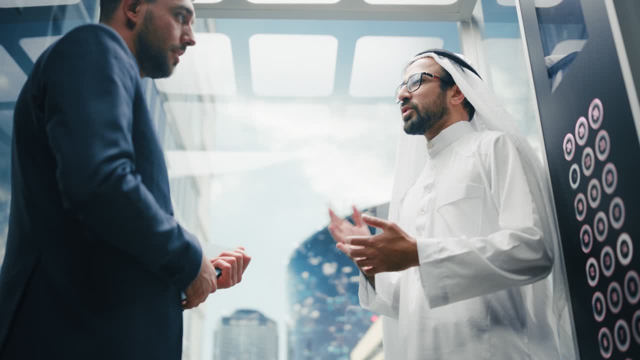 현대 비즈니스 센터의 유리 엘리베이터를 타고 사무실로 가는 동안 아랍 투자 파트너와 대화하는 사업가.
