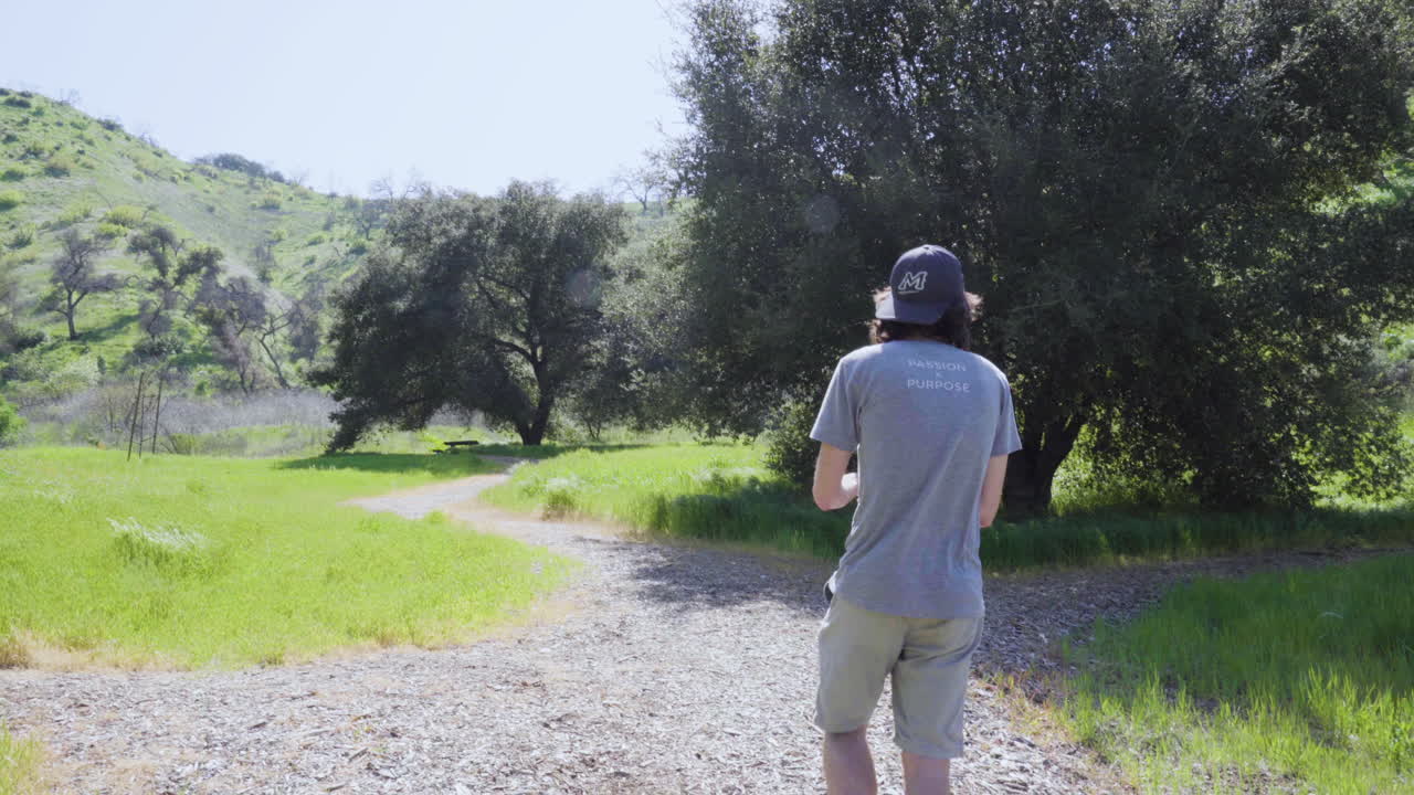 젊은 남성 영화 제작자가 짐벌을 사용하여 공원의 풍경을 부드럽게 촬영하고 있습니다.