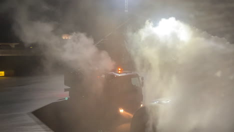 static shot of a commercial passenger aircraft being deiced at night with mist and steam billowing off the wing