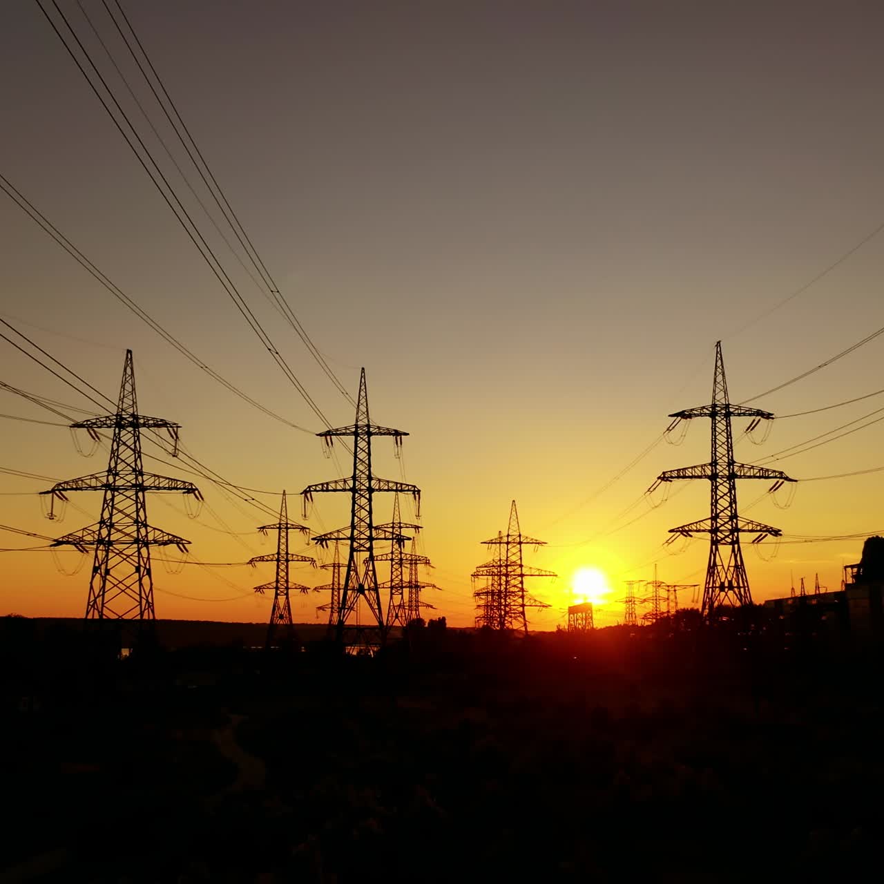 Electric pylons against orange sunset. Dark background of high-voltage electric lines in the evening. Transmission lines on the setting sun.