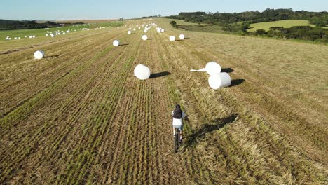 Cyclist-on-an-agricultural-field-with-hay-bales,-drone-view