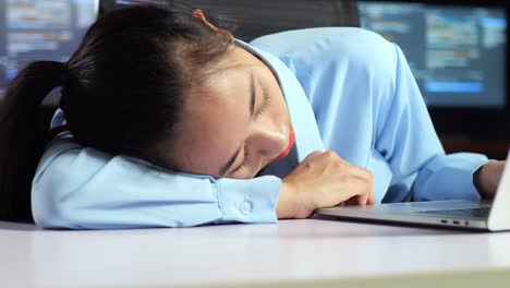 close up of asian female programmer sleeping while writing code by a laptop using multiple monitors showing database on terminal window desktops in the office