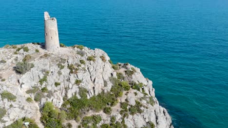 drone vuela sobre una torre de vigilancia costera, torre centenaria en el acantilado azul del mar y rocas en una hermosa vista