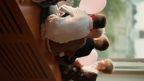 Vertical-video-of-preschool-children-sitting-on-the-windowsill-and-looking-out-the-large-window-at-the-city.-During-a-break-between-classes,-children-look-out-the-window-and-sit-on-the-windowsill