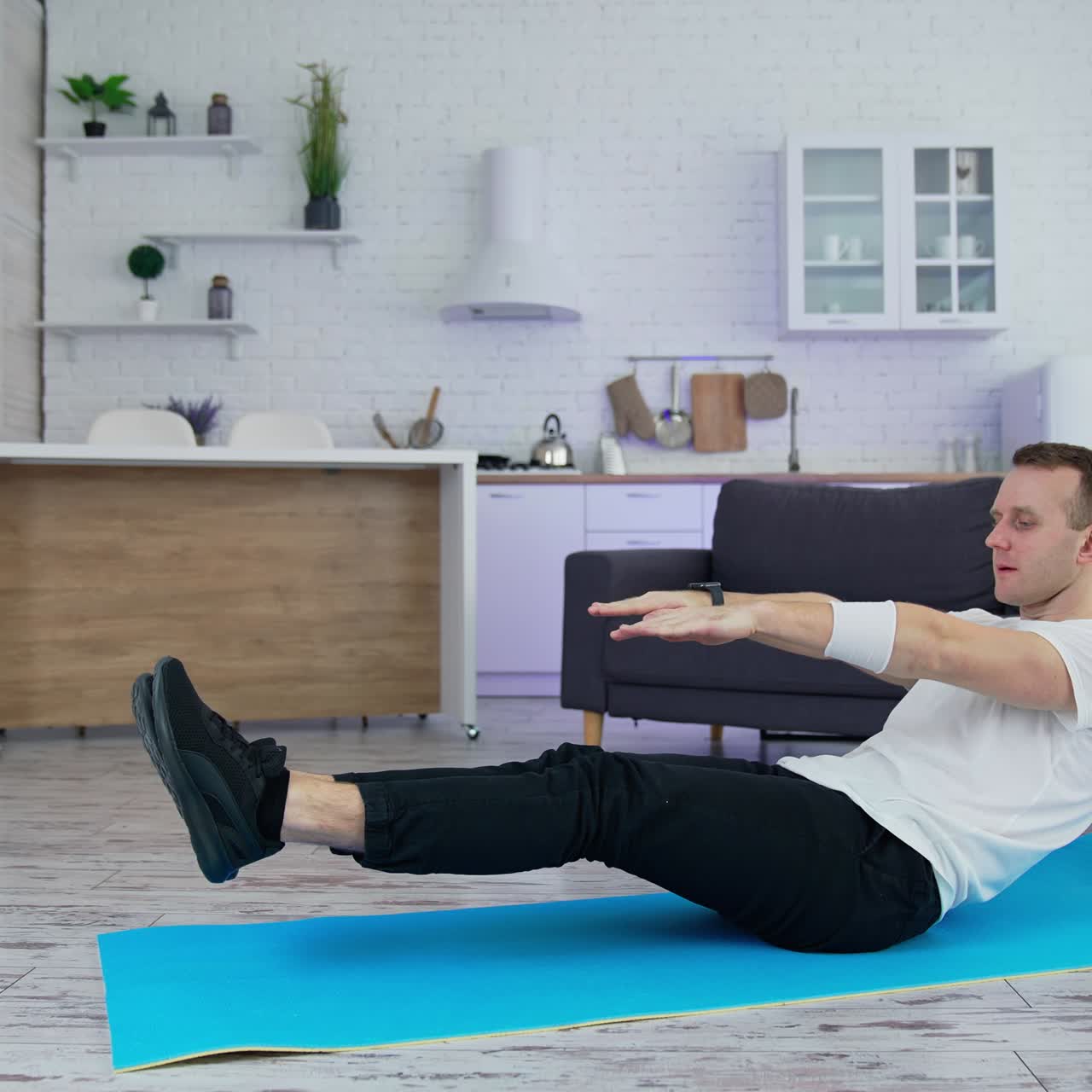 Man doing physical exercise at home. Young man practices on a mat in the modern kitchen during quarantine. Sport at home