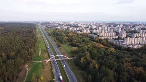 drone slowly flying towards kaunas city residential district over the a1 highway with heavy traffic and pedestrian bridge in the distance