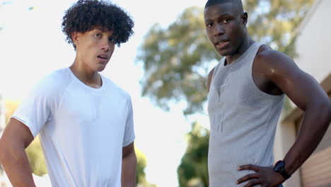 exercising outdoors, two multiracial male friends taking break and looking at camera