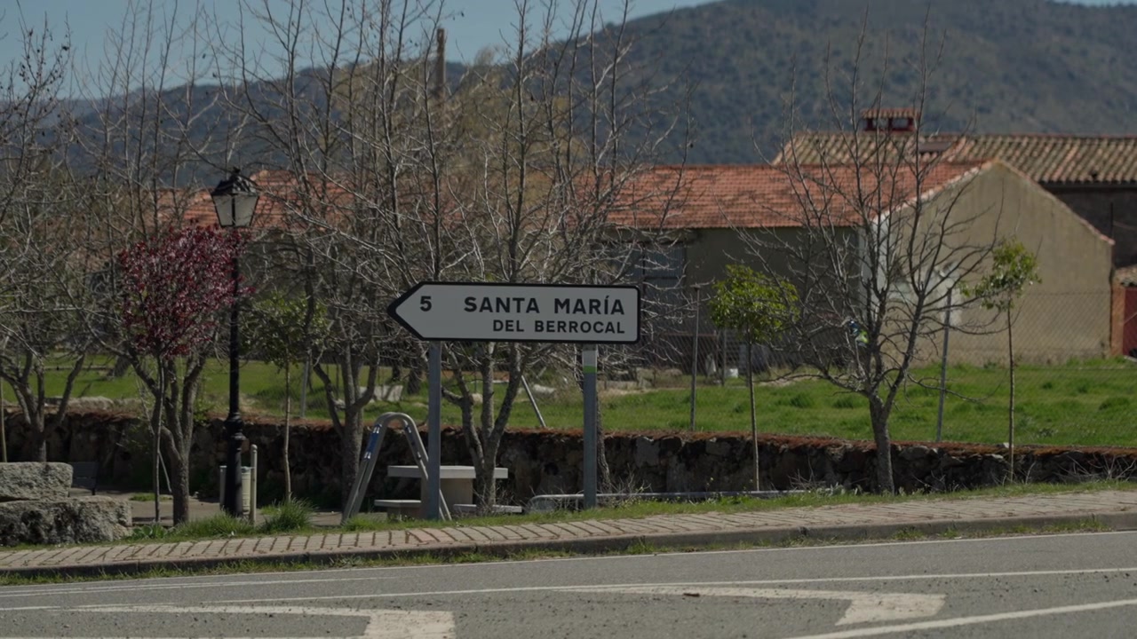 Segnale stradale di un villaggio rurale spagnolo che indica un viaggio, rappresentando il viaggio e l'architettura tradizionale in un paesaggio soleggiato.