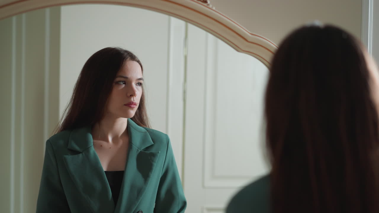 Pensive woman stands by mirror. Brunette lady has issues with self esteem evaluating looks in reflection at home. Mental state disorder symptoms