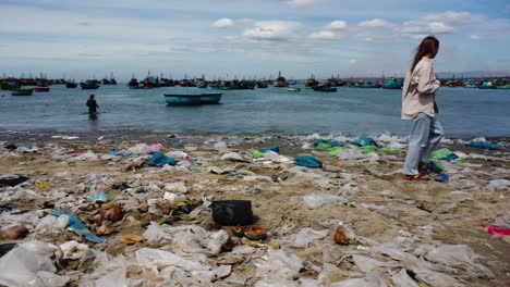 triste mujer joven caminando en la playa de arena cubierta de montones de basura, vista panorámica derecha