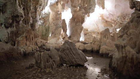 Höhlenuntergrund-Aus-Kalkstein-Mit-Weißen-Stalaktiten-Und-Stalagmiten,-Die-Durch-Einen-Beleuchteten-Tunnel-Reiten