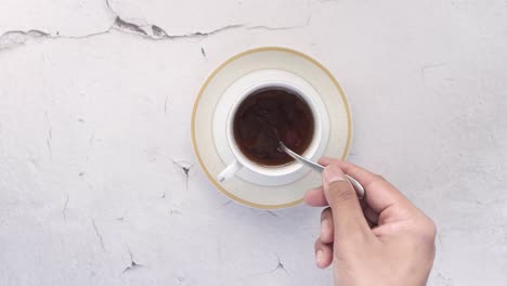 hand holding spoon with sugar in tea cup