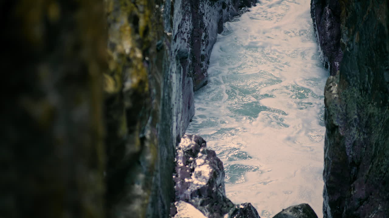 Waves breaking at ocean cliff surface closeup. Sea foaming between rocks nature