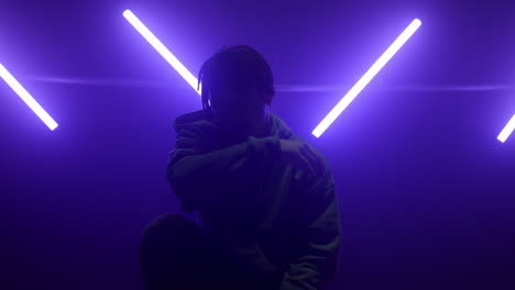 silhouette man posing illuminated ultraviolet lamps. dreads guy wiping face.