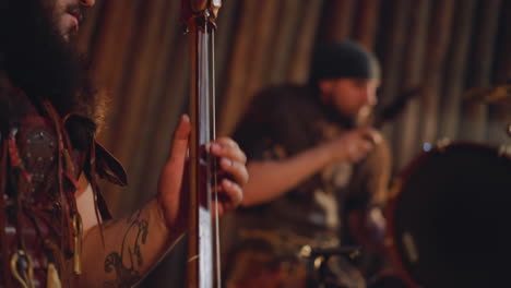 musician plays string instrument groupmate taps drums