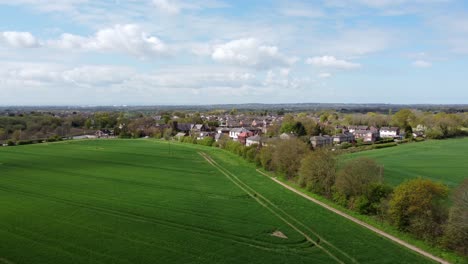 Aerial-view-approaching-rural-British-countryside-village-suburbs-surrounded-by-farmland-fields,-Cheshire,-England