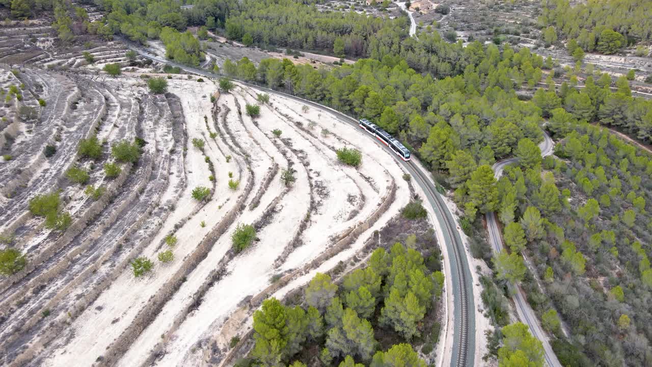 A train winds through a green forest and sandy landscape in Calpe, Spain, aerial view