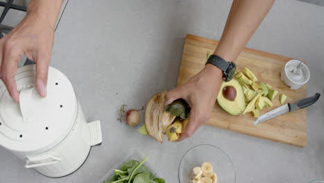 hands of senior biracial man preparing smoothie, composting bio waste in kitchen, slow motion