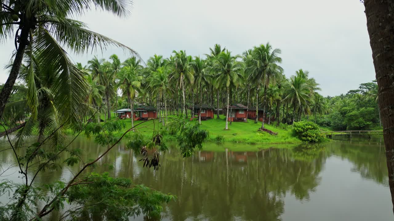 From the front of a tranquil lake in Laguna, the camera moves upward and forward, highlighting traditional bahay kubo houses and the surrounding greenery