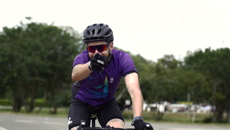 cyclist points at the camera while he drives his bicycle on the street