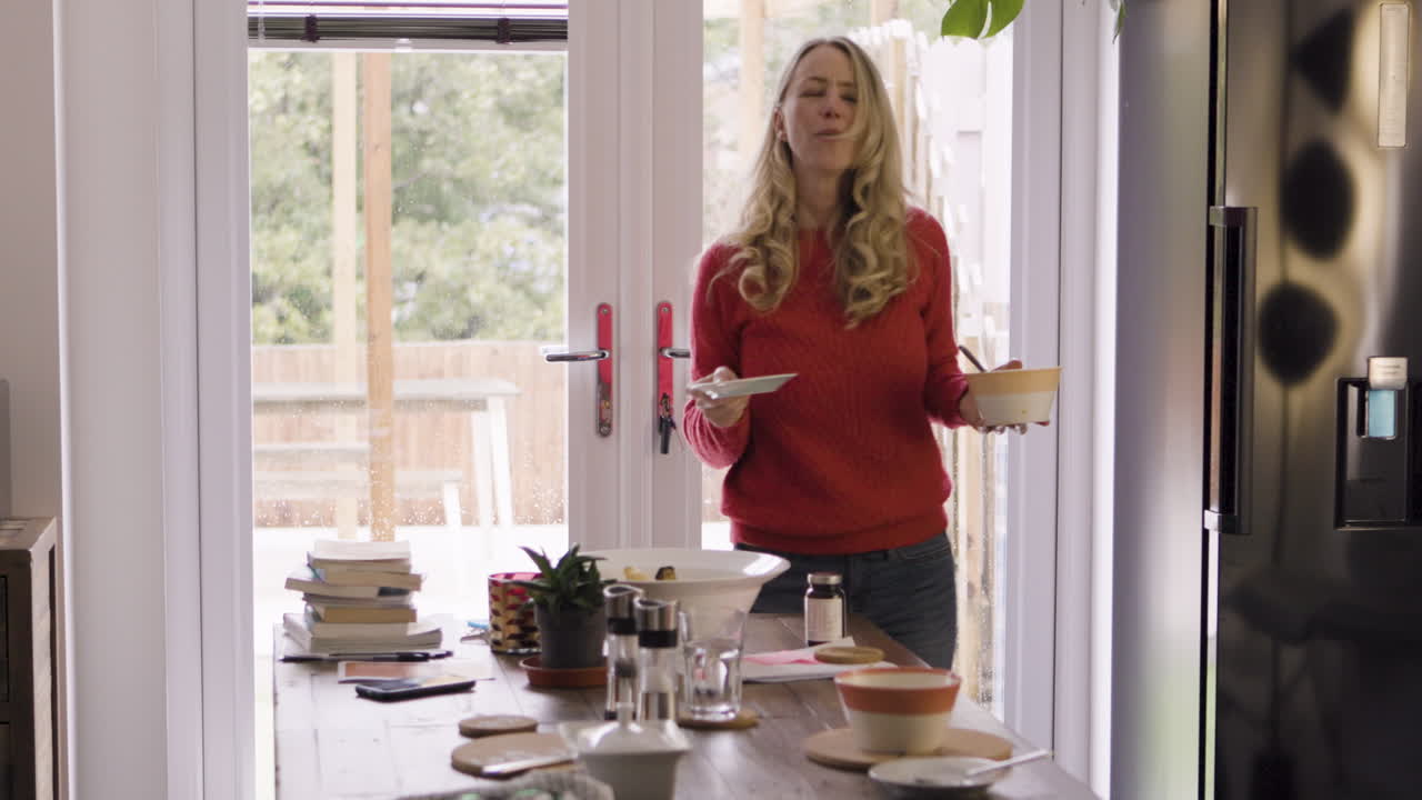 A woman in a kitchen near a dining table and refrigerator