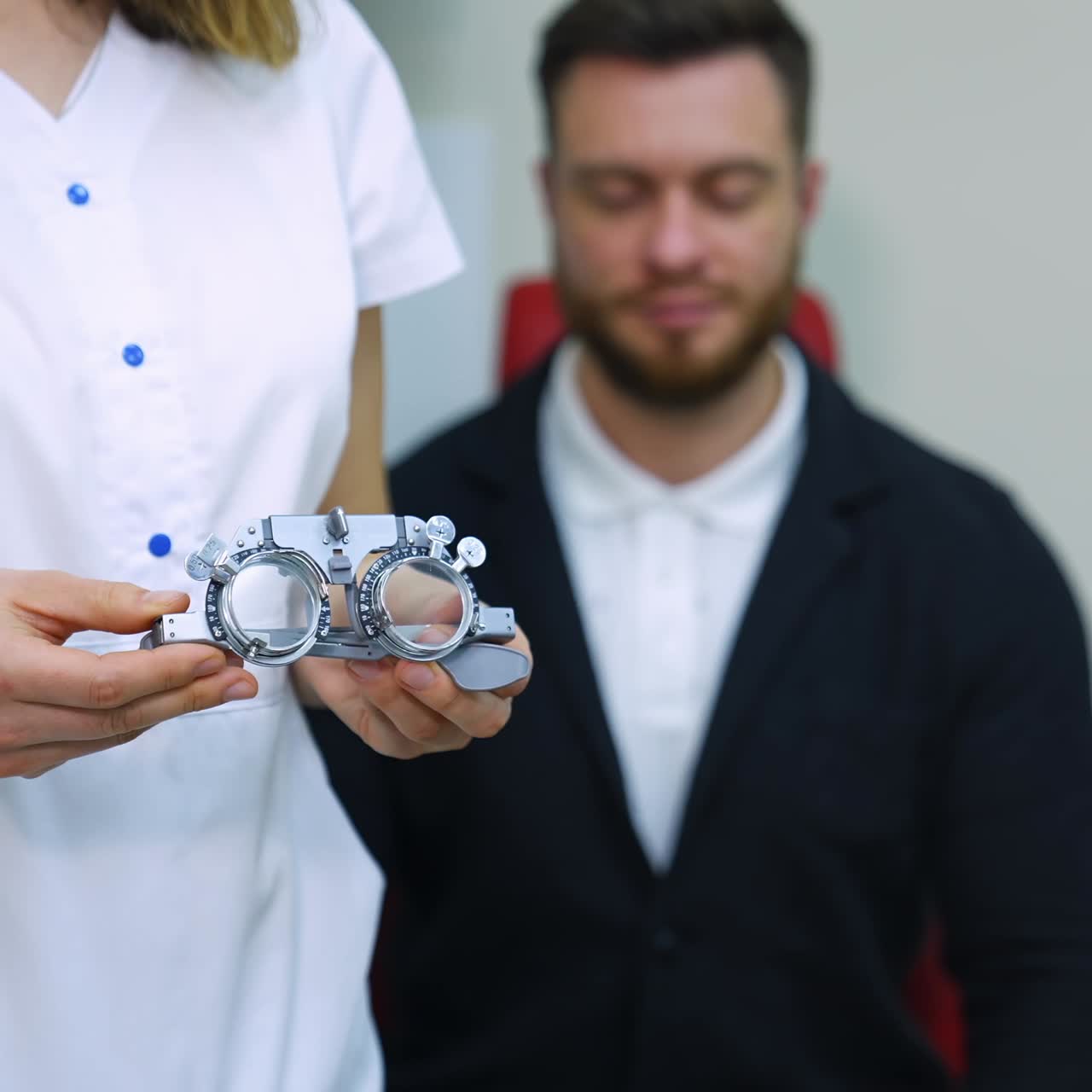 Testing glasses in doctor's hands. Ophthalmologist in medical gown standing near the patient and holding trial frame glasses in clinic. Eyesight concept