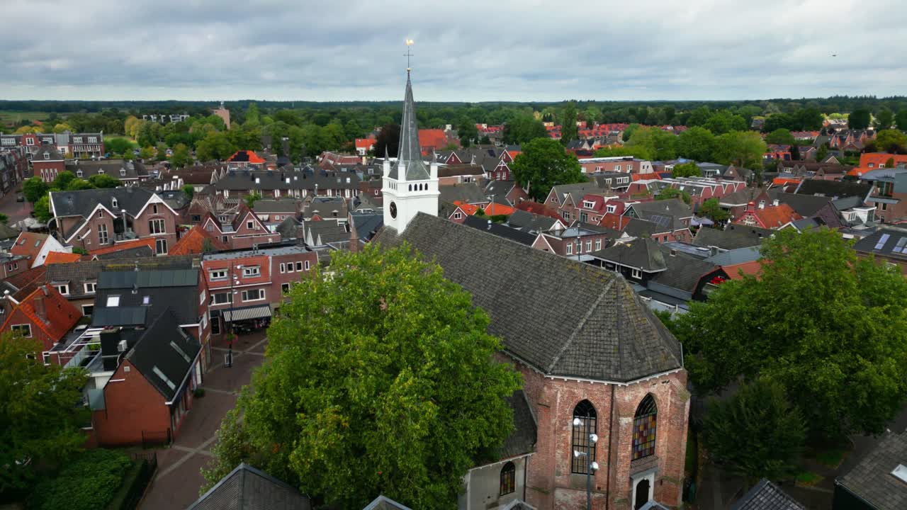 Drone shot of historic brick church encircled by narrow streets, houses, and green trees. Captured in Ommen, Overijssel, Netherlands (Ommen, Overijssel, Nederland)