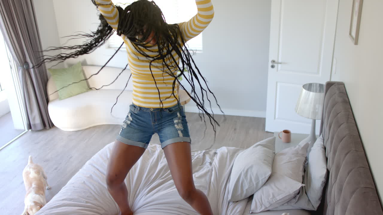 African American young woman dancing on bed, hair flying, at home