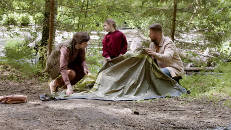 young family setting up tent near the river