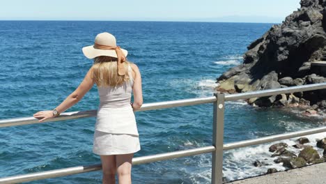 Attractive-blonde-woman-standing-near-Atlantic-ocean-coastline,-back-view