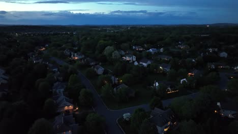 tilt up drone shot of quiet american neighborhood at dusk. night scene with lighting houses in suburbia. wide shot. quaint housing area with illuminated windows.