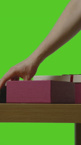 vertical video of man putting present into gift wrapped box on table shot against green screen 2