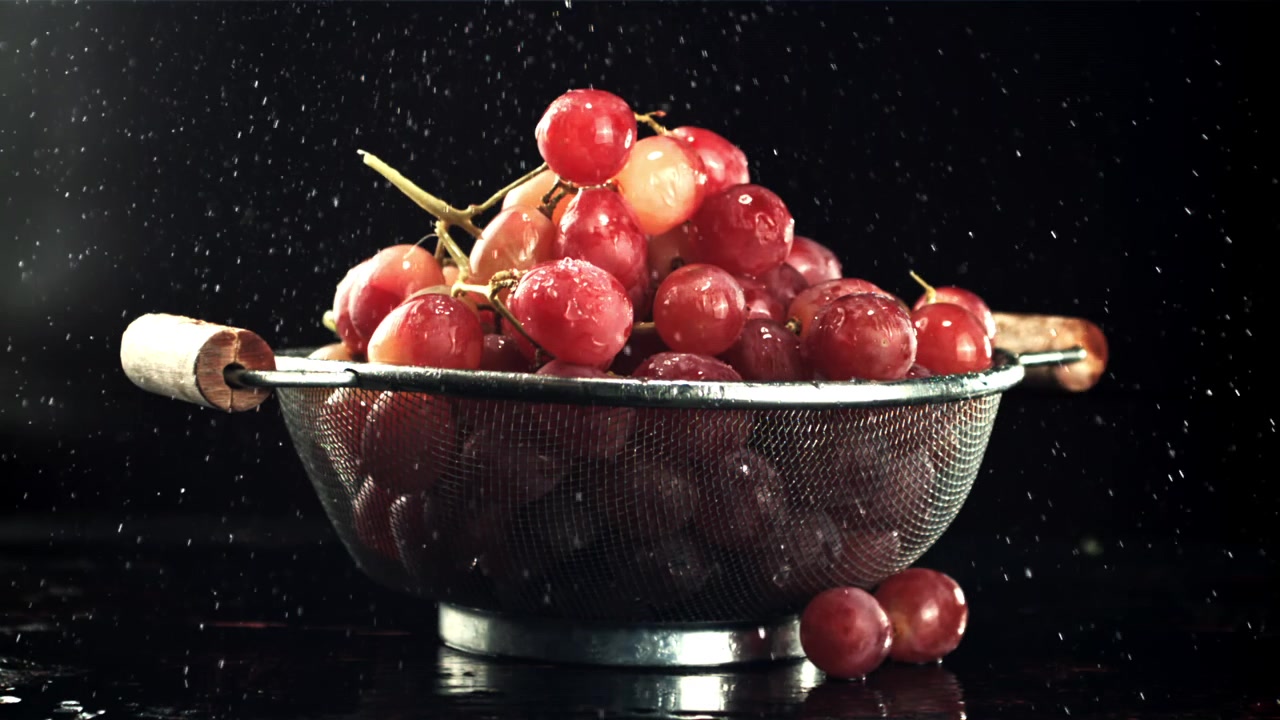 Uva rossa fresca che si sciacqua in uno scolapasta di metallo con goccioline d'acqua