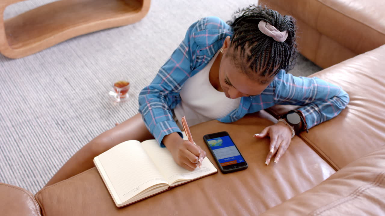 African American young woman wearing blue plaid shirt, writing in a notebook