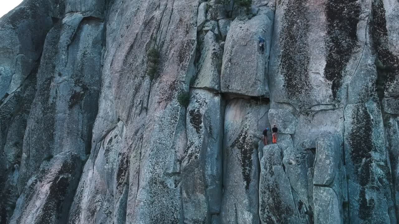 Aerial ascending shot of a granite wall showing at last three tiny climbers on it