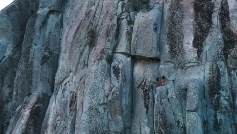 aerial ascending shot of a granite wall showing at last three tiny climbers on it
