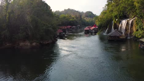 una maravillosa toma aérea rotacional de drones de 4k de un río en la jungla de tailandia, mirando un pequeño y encantador pueblo flotante y una hermosa cascada en el parque nacional sai yok en asia