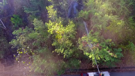 Aerial-view-of-a-firetruck-using-the-ladder-hose,-to-extinguish-of-tropical-forest-fire---descending,-tilt-up,-drone-shot