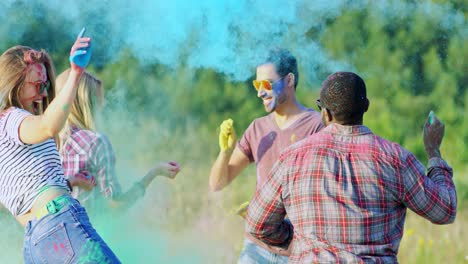 jóvenes multiétnicos felices y alegres rociando pinturas coloridas a sus novias durante el festival holi en el campo