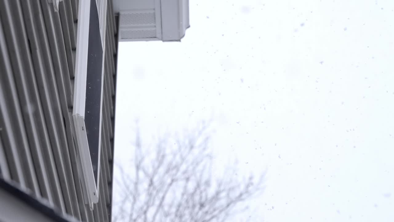 Small snowflakes falling down on a cold winter day, grey sky, slow motion, looking up on a house, copy space