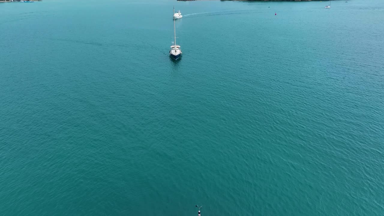 Aerial view of a tranquil sea with moored sailing boats against a backdrop of mountainous scenery.