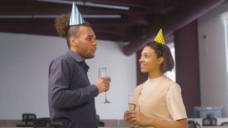 mujer americana y hombre hablando juntos, luego brindando y bebiendo champán en la fiesta de la oficina