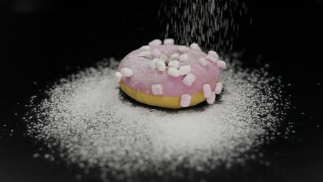 tasty fresh donut lay on black surface and gets sprinkle with icing sugar powder