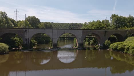 person standing on the foot path of a train trestle that leads over a green river in the countryside of germany