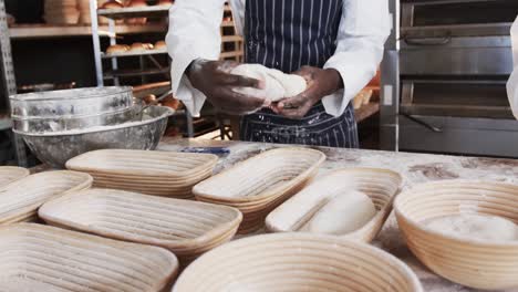 midsection of diverse bakers working in bakery kitchen, forming bread form dough, slow motion