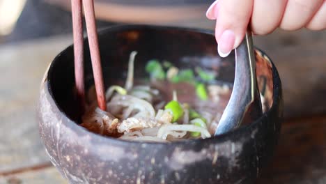 savoring noodle dish in coconut shell bowl